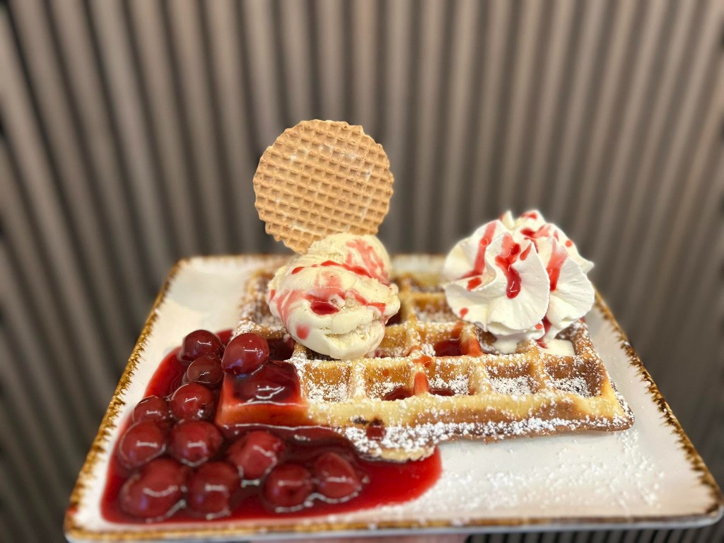 Frische Waffel mit Vanilleeis, heißen Kirschen und Schlagsahne im Eis-Café Caramello